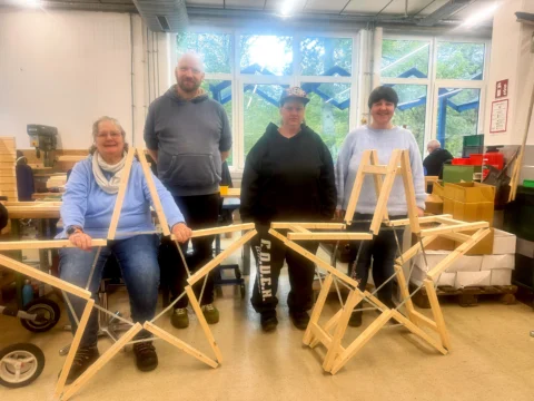 Vier Menschen in einer Werkstatt zeigen zwei verschiedene Holzsterne.