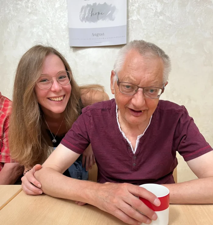 Älterer Mann und junge Frau lächeln am Tisch mit Kaffeetasse, Familienbesuch.