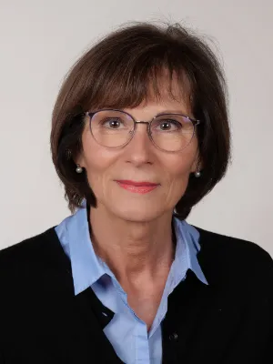 Business-Porträt einer Frau mit Brille, blauem Hemd und schwarzer Strickjacke.