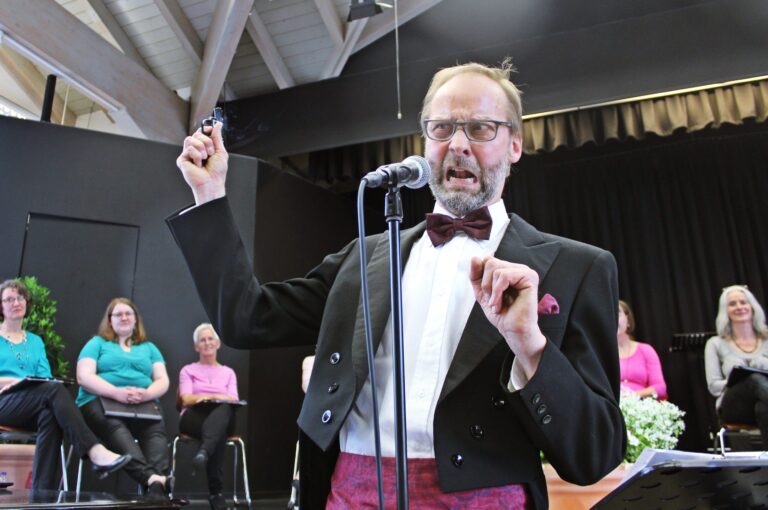 Bariton Andreas Balzer mit humorvoller Mimik am Mikrofon bei Benefizkonzert auf der Bühne.