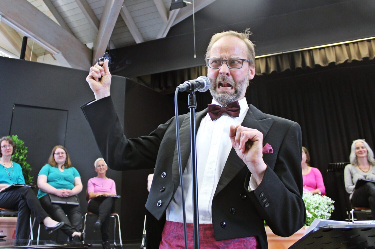 Bariton Andreas Balzer mit humorvoller Mimik am Mikrofon bei Benefizkonzert auf der Bühne.