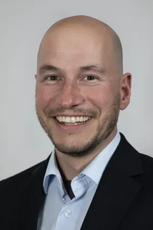 Professionelles Business-Porträt von Benjamin Weyerich, lächelnder Mann im Anzug vor grauem Hintergrund.