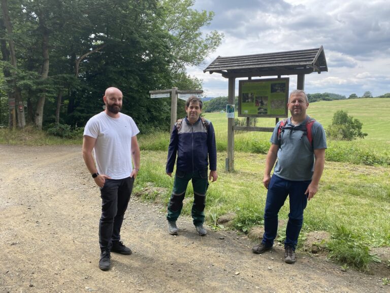Drei Männer starten begleiteten Ausflug im betreuten Wohnen am Waldweg mit Infotafel.