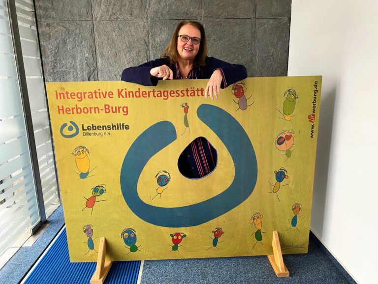 Conny Müller verabschiedet sich nach 48 Jahren bei Lebenshilfe Dillenburg vor Kita-Schild.