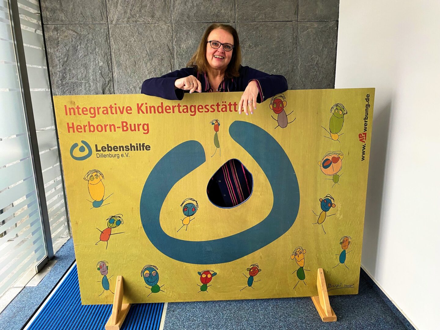 Conny Müller verabschiedet sich nach 48 Jahren bei Lebenshilfe Dillenburg vor Kita-Schild.