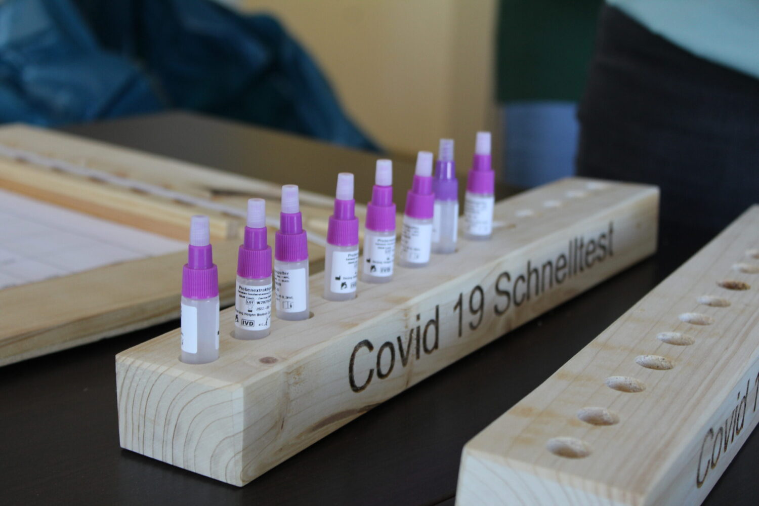 Probenröhrchen für Covid-19-Schnelltests in Holzhalter auf Teststationstisch.