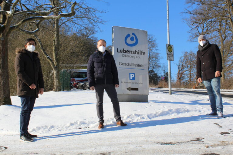 Spendenübergabe vor der Lebenshilfe Dillenburg: drei Männer mit Maske im Schnee neben Firmenschild.