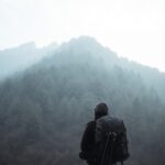 Einsamer Wanderer mit Rucksack blickt auf nebligen Bergwald und Gipfel.