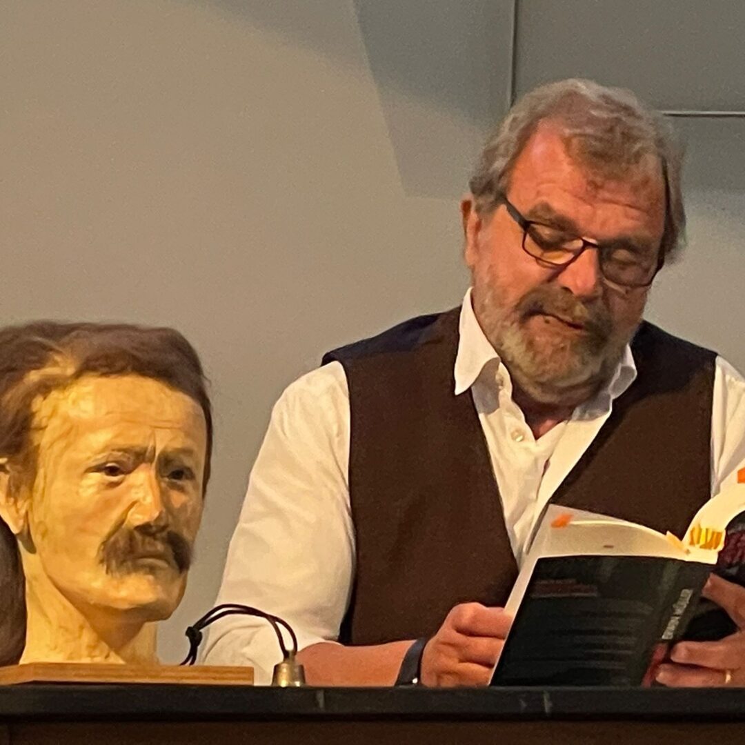 Erwin Müller liest Krimi, daneben Gesichtsrekonstruktion des unbekannten Toten auf dem Podium.