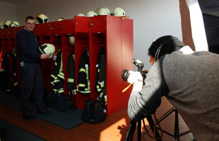 Feuerwehrmann in Haiger posiert mit Helm vor Spinden, Fotograf nimmt Einsatzkleidung auf.