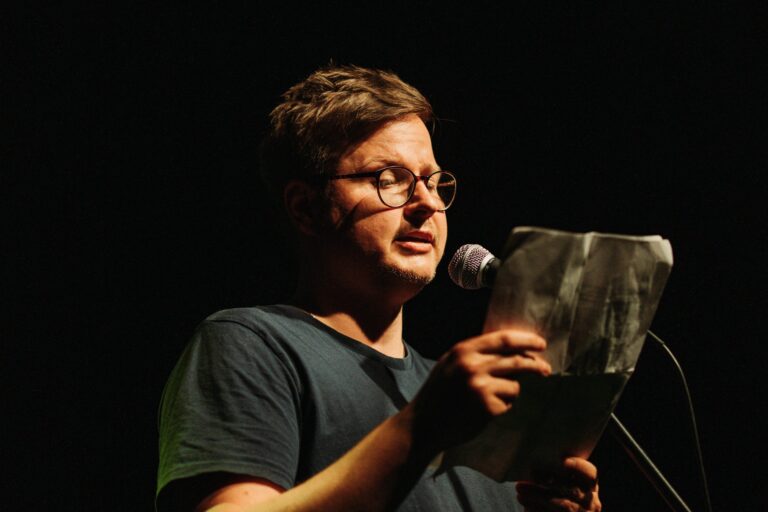 Florian Wintels liest beim Scheunen-Slam Herborn 2024 am Mikrofon unter Spotlight.