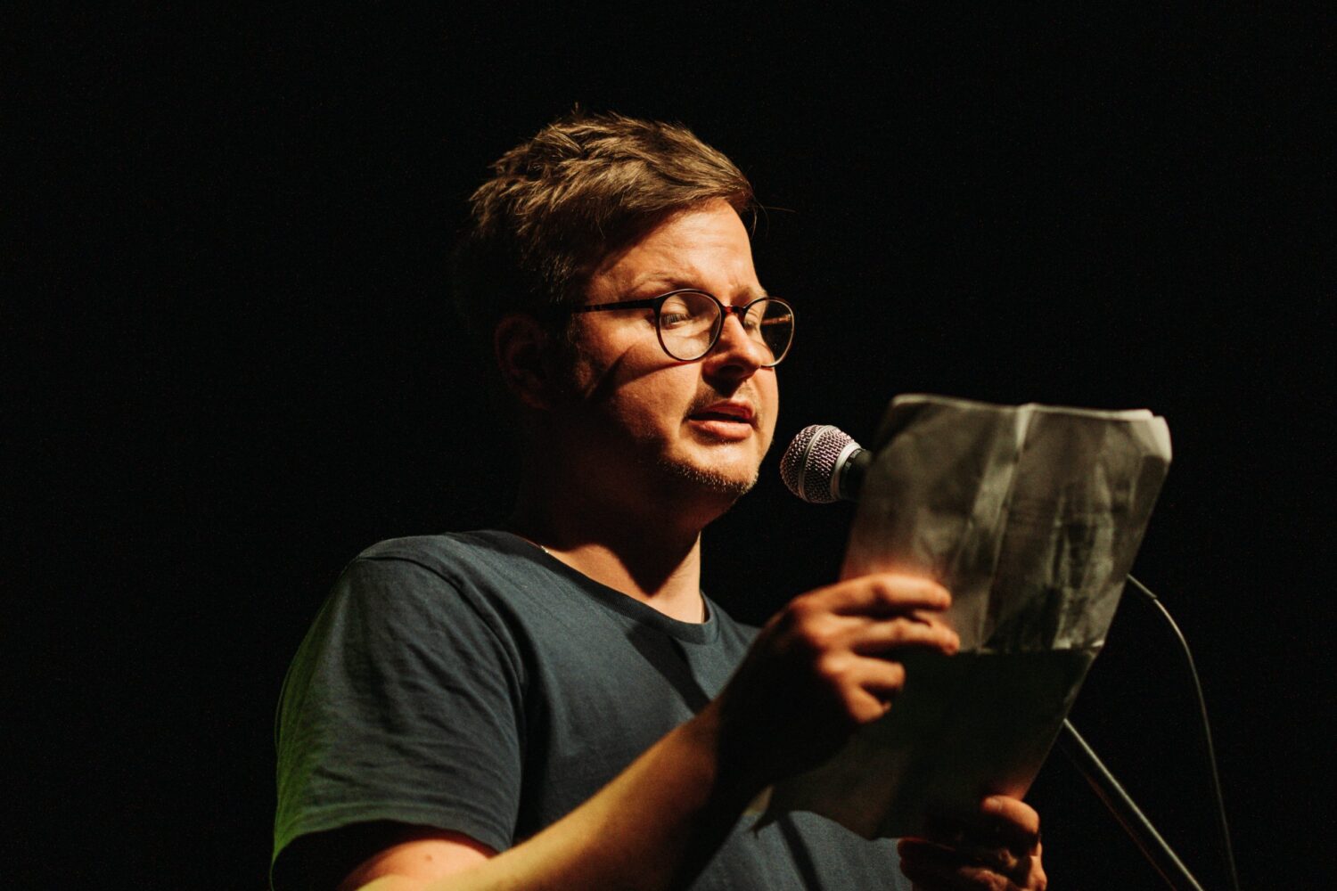 Florian Wintels liest beim Scheunen-Slam Herborn 2024 am Mikrofon unter Spotlight.