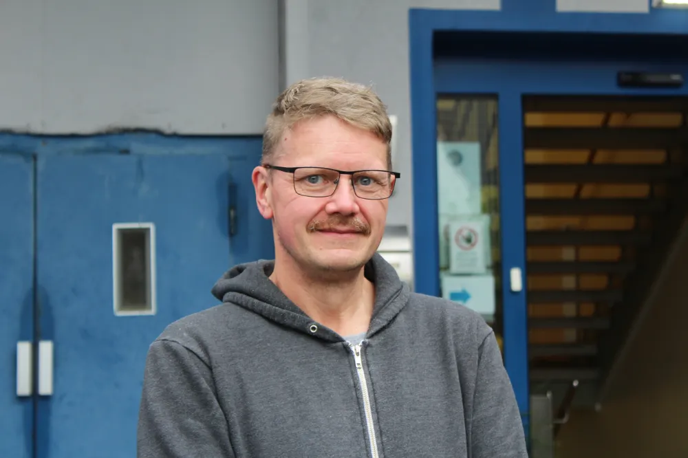 Porträt eines Mannes mit Brille vor blauem Gebäudeeingang im Freien