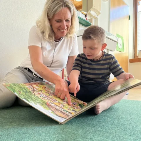 Frau liest mit Kind ein Bilderbuch im Kindergarten, frühe Bildung und Sprachförderung.