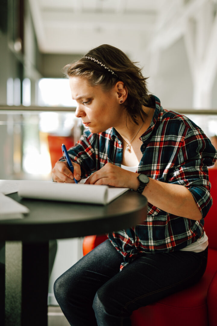 Junge Frau schreibt konzentriert Notizen am Tisch in hellem Café-Lernbereich.