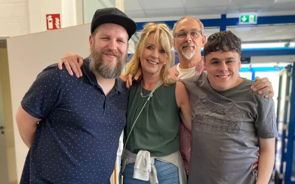 Vier Freunde lächeln in hellem Innenraum, Gruppenfoto bei Gemeinschaftstreffen.