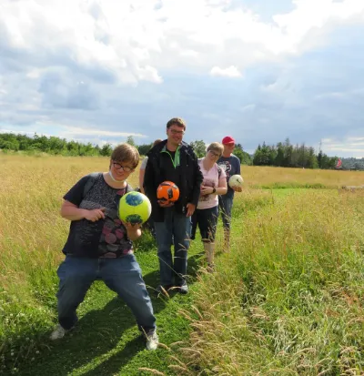 Freunde mit Fußbällen auf Wiesenpfad im Feld unter blauem Himmel.