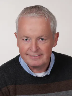 Freundliches Business-Porträt eines älteren Mannes mit grauen Haaren und blauem Hemd.