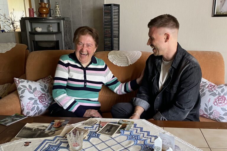 Großmutter und Enkel lachen gemeinsam auf dem Sofa, alte Familienfotos auf dem Tisch.