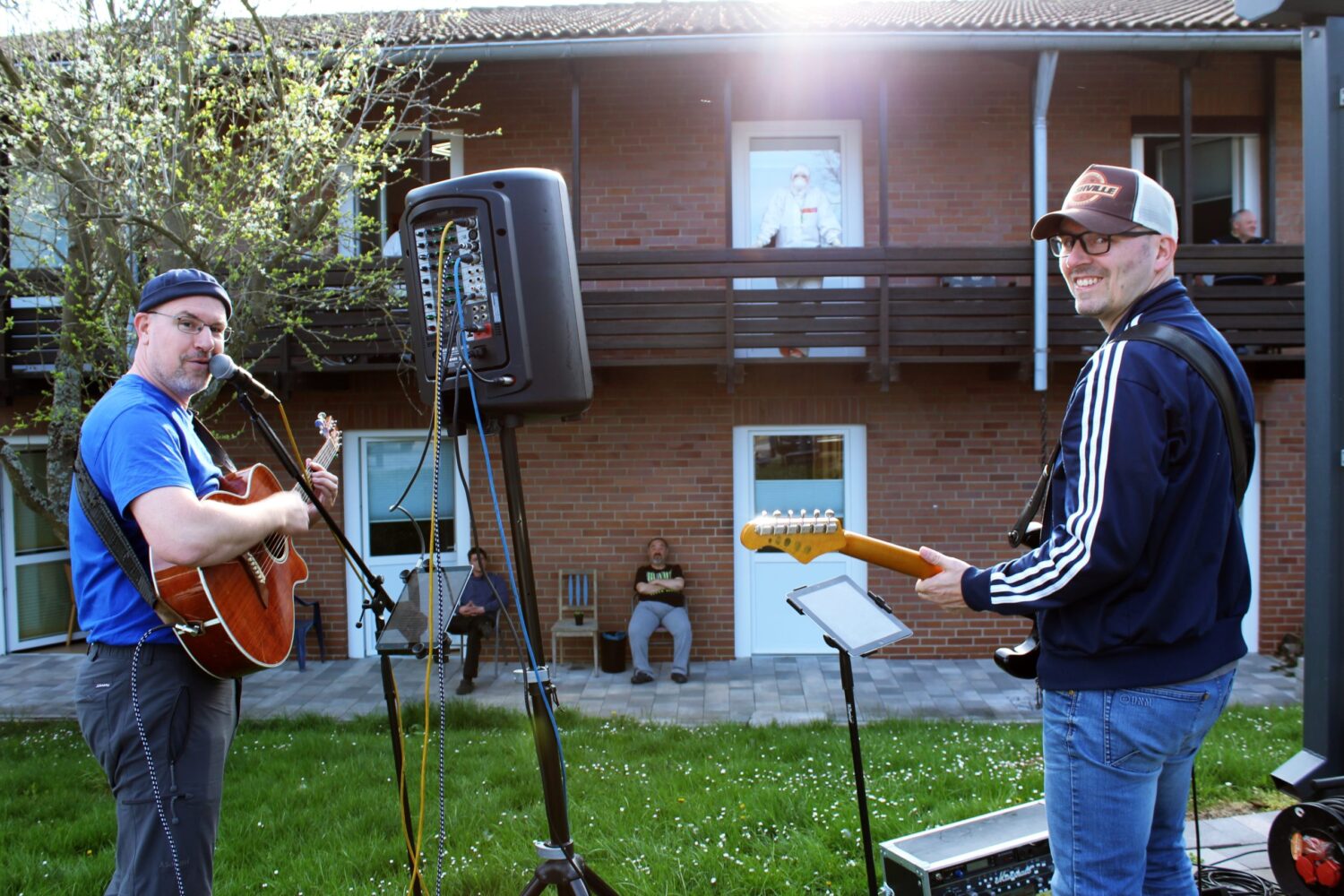 Gitarren-Duo spielt Outdoor-Konzert im Wohnheim Niederscheld, Bewohner schauen zu.