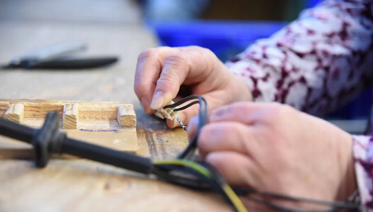 Hände verbinden Elektrokabel an Werkbank, präzise Elektroinstallation und Reparaturarbeit.