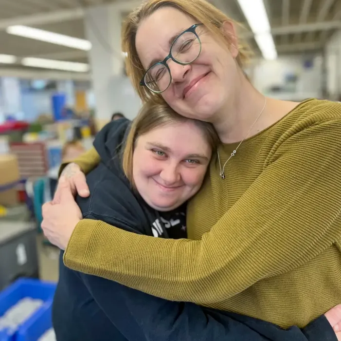 Zwei Frauen umarmen sich herzlich im Büro, Freundschaft und emotionaler Zusammenhalt.