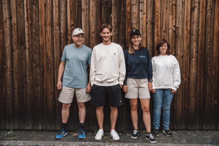 Vier Models präsentieren Lebenshilfe-Kollektion vor rustikaler Holzwand beim inklusiven Fotoshooting.