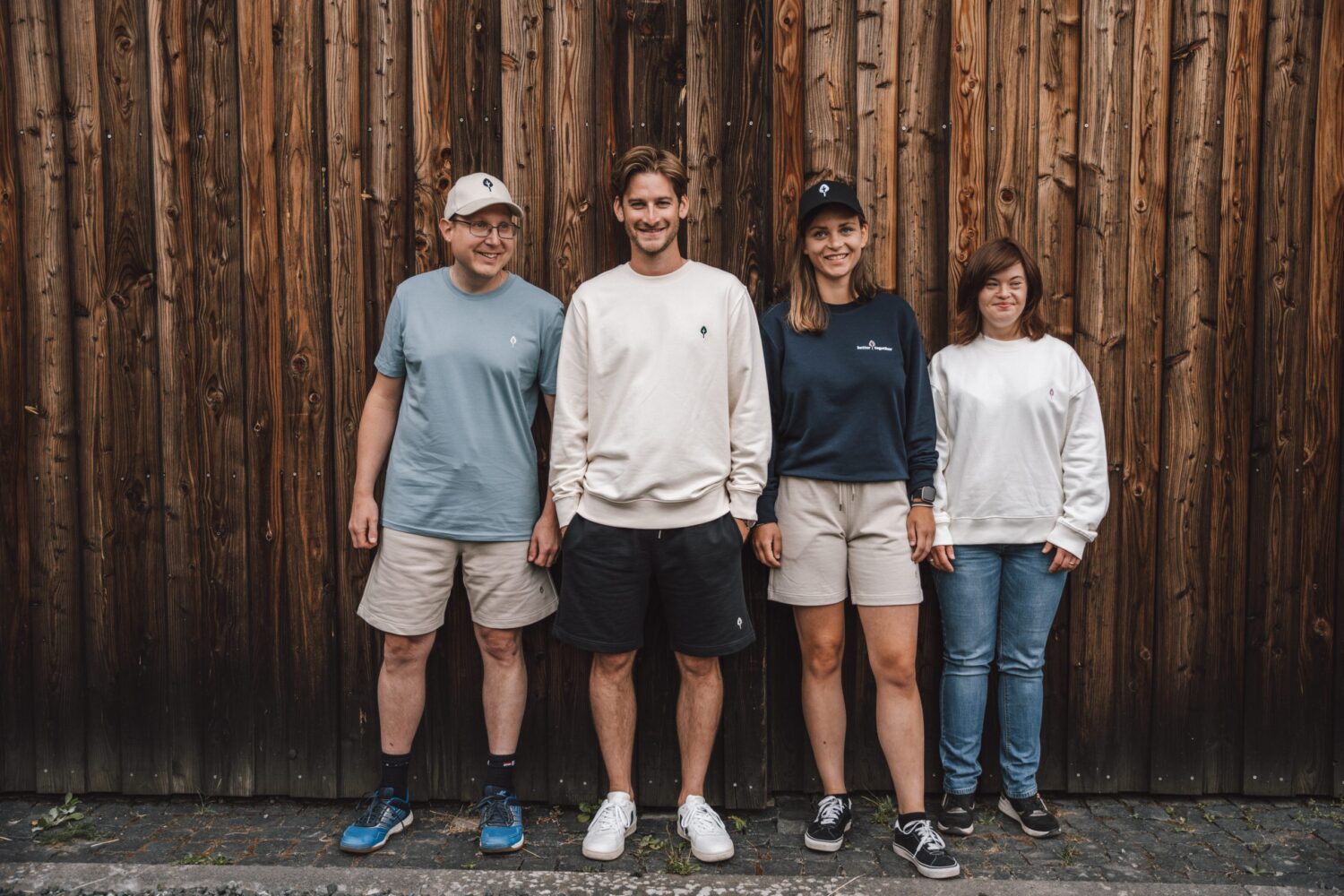 Vier Models präsentieren Lebenshilfe-Kollektion vor rustikaler Holzwand beim inklusiven Fotoshooting.