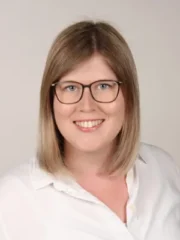 Professionelles Porträt von Isabel Jung mit Brille, blondem Haar und weißer Bluse.