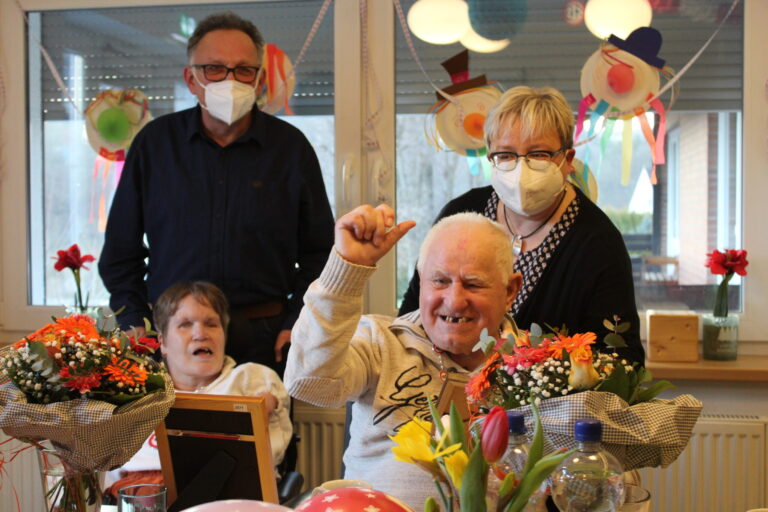 Geschenke zum Jubiläum im Seniorenheim: Bewohner mit Blumen, Pflegende gratulieren im Festsaal.