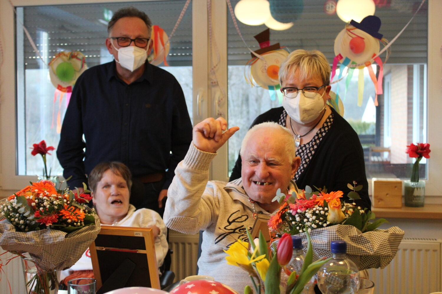 Geschenke zum Jubiläum im Seniorenheim: Bewohner mit Blumen, Pflegende gratulieren im Festsaal.