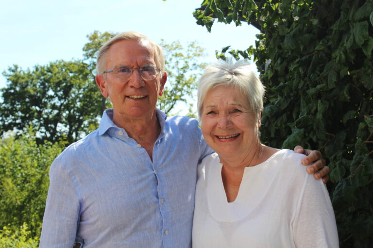 Jürgen und Sigrid Raab lächeln im Garten, eng umarmt, sonniger Tag.