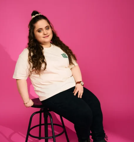 Junge Frau auf schwarzem Hocker vor pinkem Hintergrund im Fotostudio Porträt