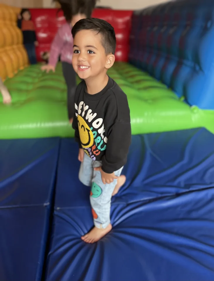 Fröhlicher Junge lächelt barfuß in bunter Indoor-Hüpfburg und spielt ausgelassen.