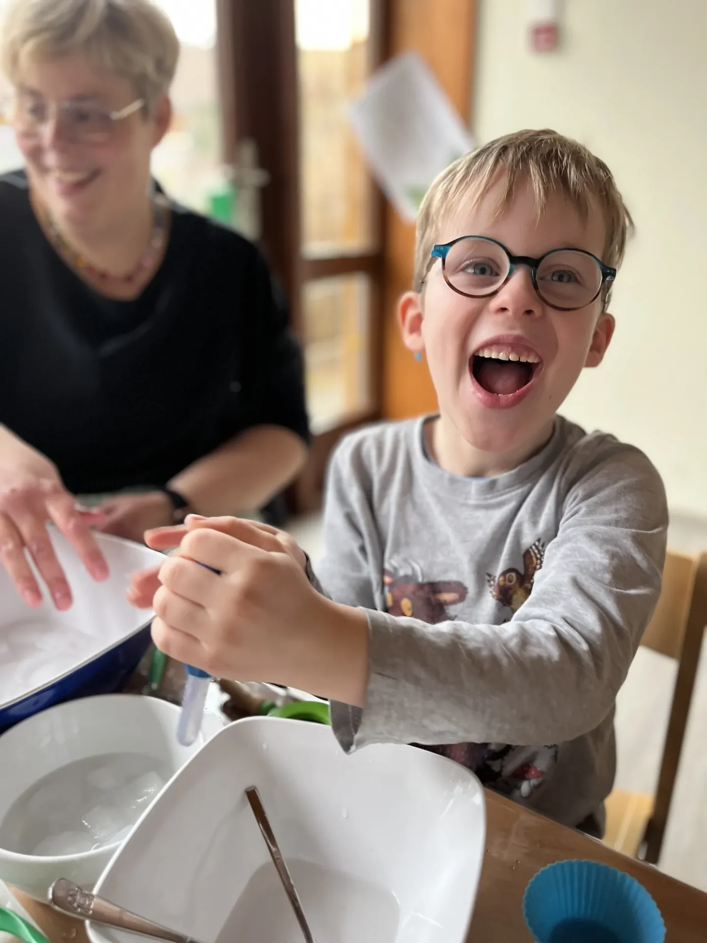 Fröhlicher Junge mit Brille experimentiert mit Wasser in Schüsseln am Tisch.
