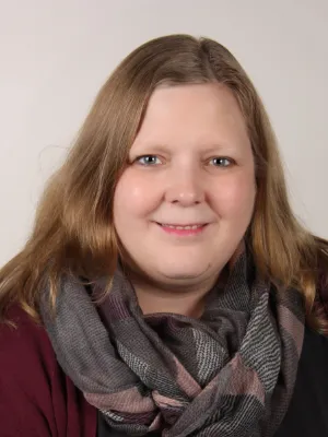 Porträt von Katharina Warburg mit Schal, professionelles Profilfoto vor grauem Hintergrund.