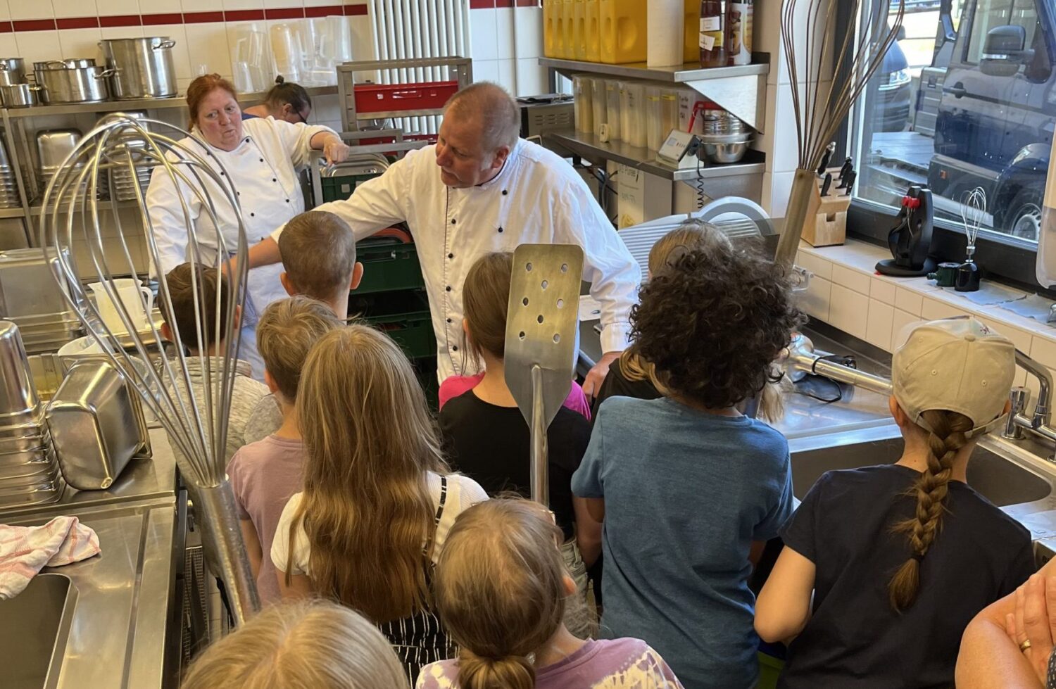 Koch erklärt Schulkindern den Ablauf in der Großküche bei einer Küchenführung.
