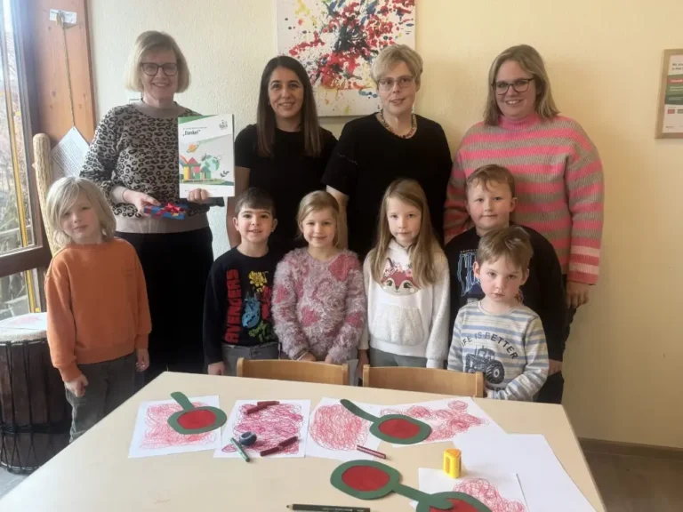 Erzieherinnen und Kita-Kinder zeigen Bastelarbeiten am Tisch im Kindergarten-Gruppenfoto.