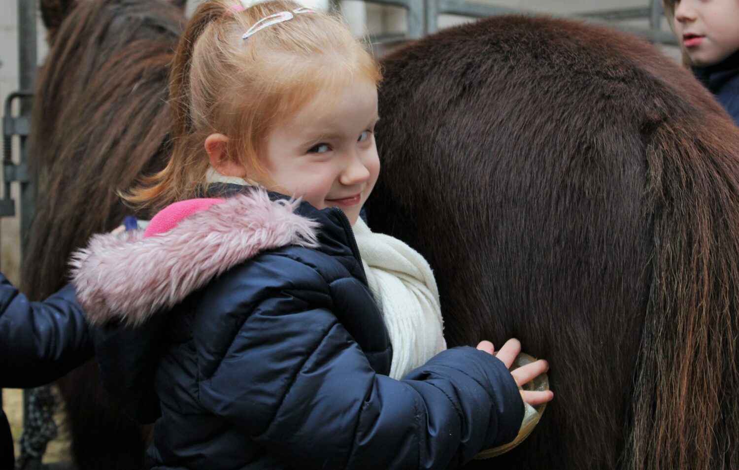 Kita-Kind streichelt Therapiepony Feivel im Stall, warm eingepackt im Winter.