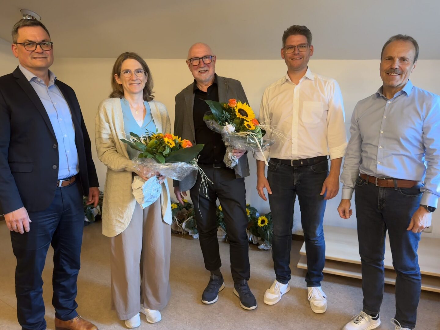 Kollegen verabschieden Jeannine Schreiner und Michael Koch mit Blumensträußen bei einer Feier.