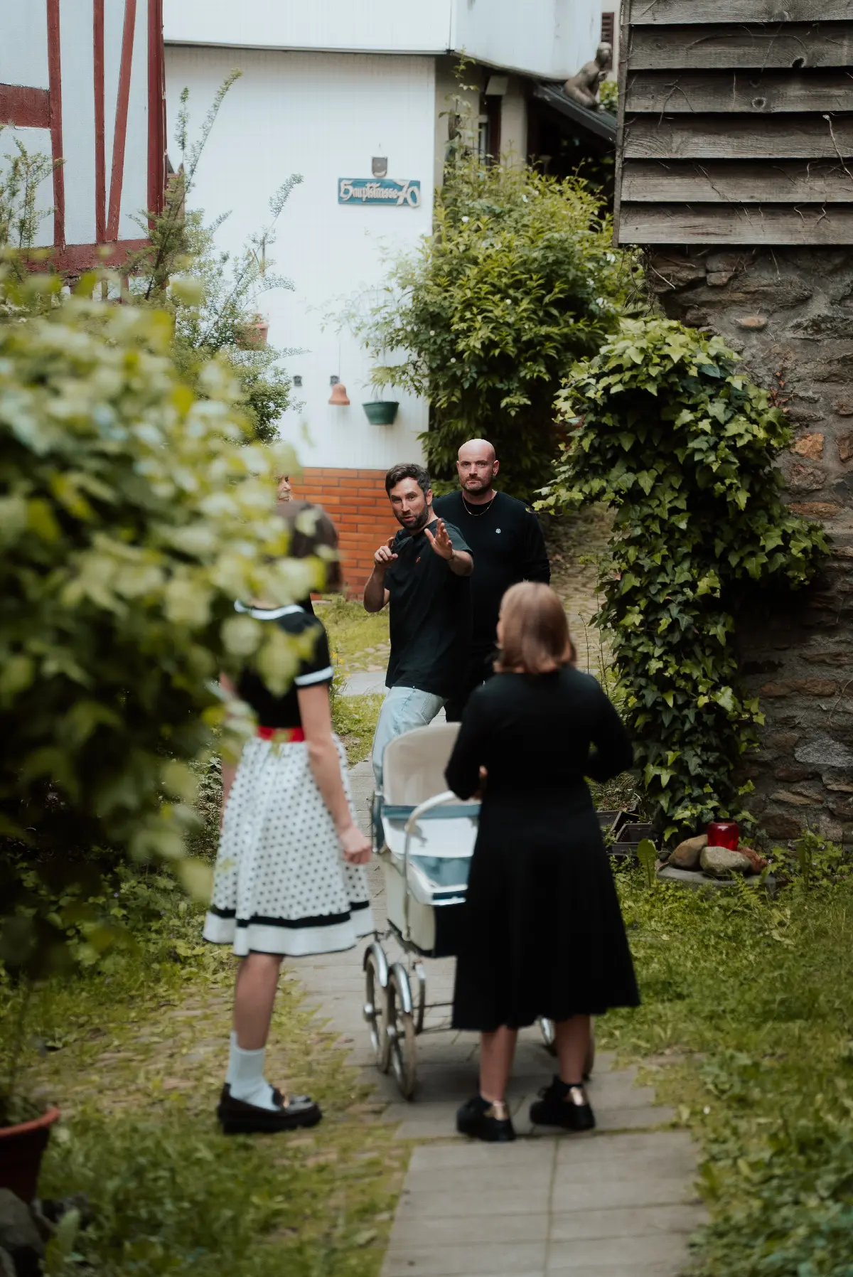 Zwei Frauen mit Vintage-Kinderwagen in idyllischer Kopfsteinpflastergasse, Männer im Hintergrund