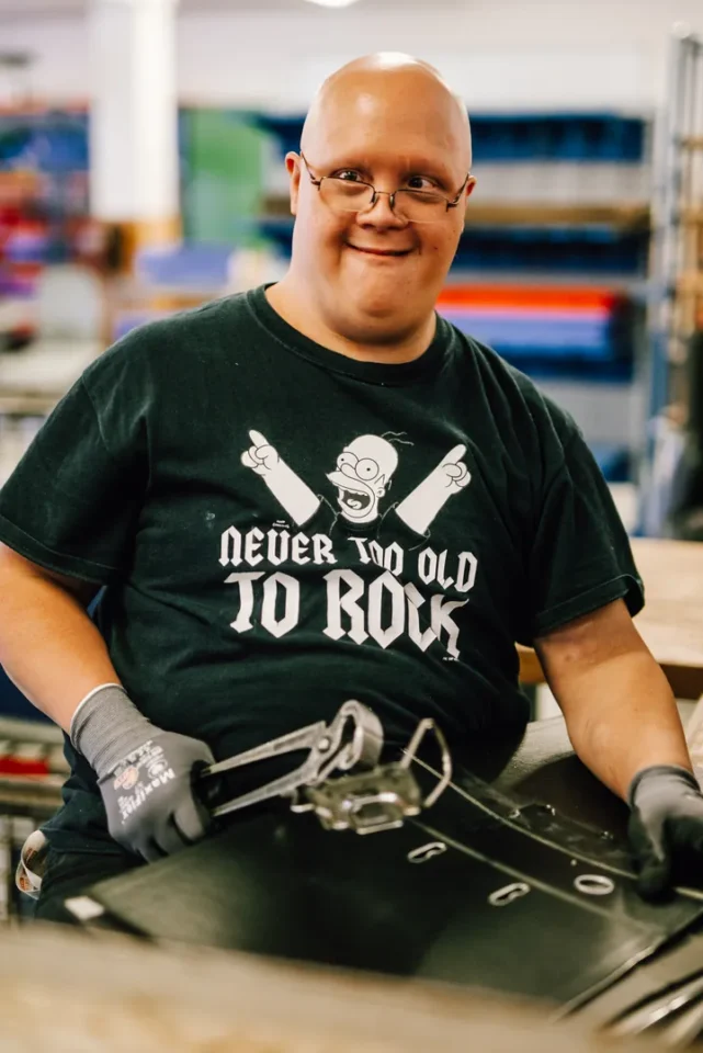 Lachender Mitarbeiter mit Brille montiert Bauteile an Werkbank in der Werkstatt.