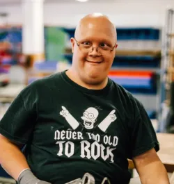 Lachender Mann mit Brille in Werkstatt, Rock-Shirt „Never Too Old to Rock“.