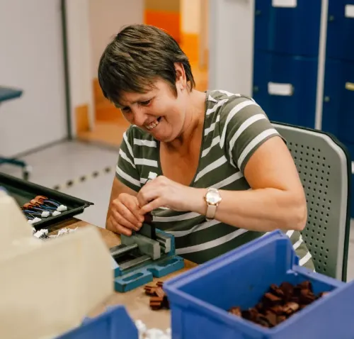 Lächelnde Frau montiert Kleinteile am Arbeitstisch in Werkstatt mit Kunststoffteilen.