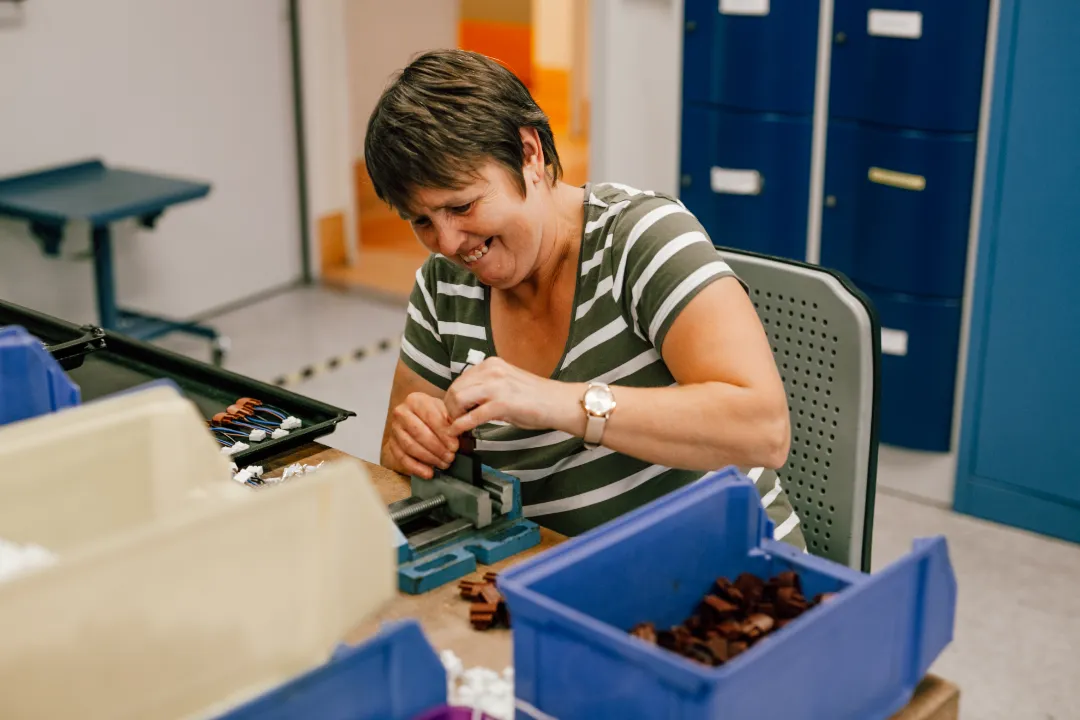 Lächelnde Mitarbeiterin montiert Kleinteile am Werktisch in moderner Werkstatt