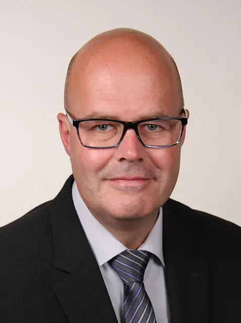 Professionelles Business-Porträt eines glatzköpfigen Mannes im Anzug mit Brille.