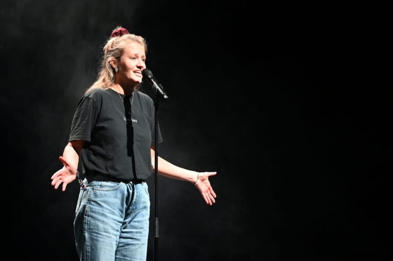 Leah Weigand auf der Bühne am Mikrofon im Scheinwerferlicht, Poetry Slam Performance.
