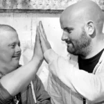 Zwei Männer geben sich einen High-Five, echte Freundschaft und Inklusion in Schwarzweiß.