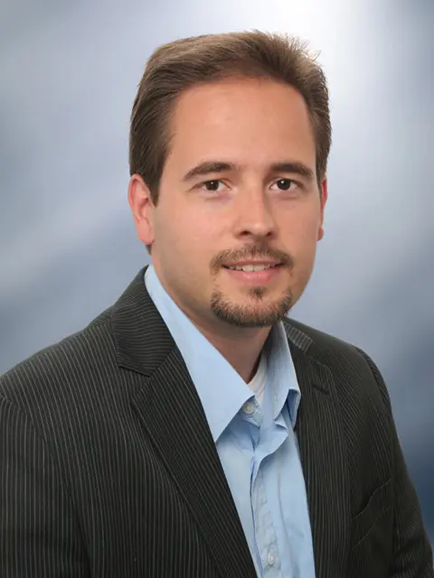 Professionelles Businessporträt eines Mannes im Anzug vor blauem Studiohintergrund.