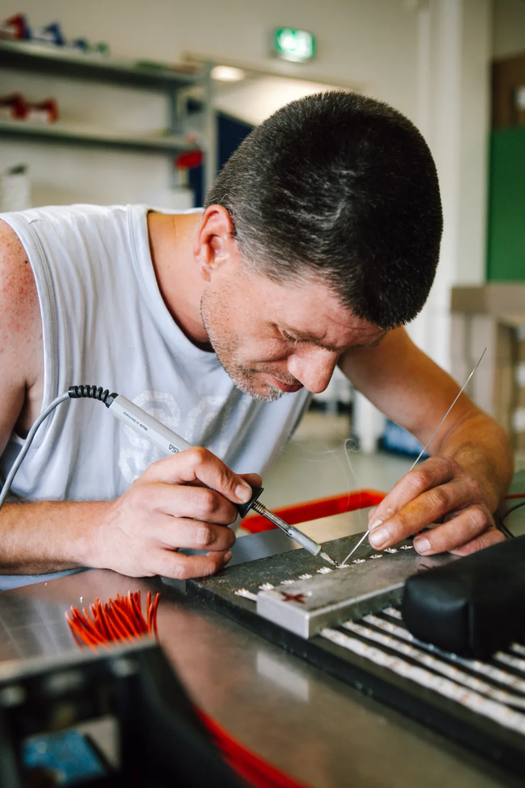 Mann lötet präzise elektronische Bauteile am Arbeitsplatz in einer Werkstatt.